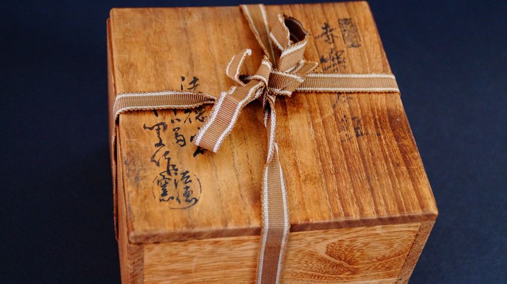 Closed storage box of the chawan made of Raku ware by Sairi Hotoku with ink inscription and artist's seal, tied with striped cord
