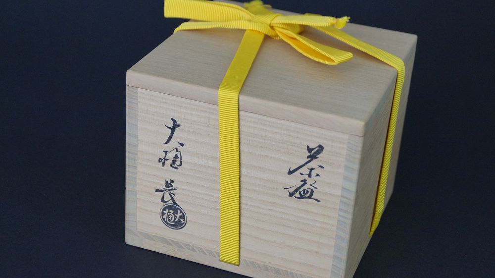 Geschlossene, mit gelbem Band verschnuerte Aufbewahrungsbox der Chawan Teeschale aus Ohi-Keramik