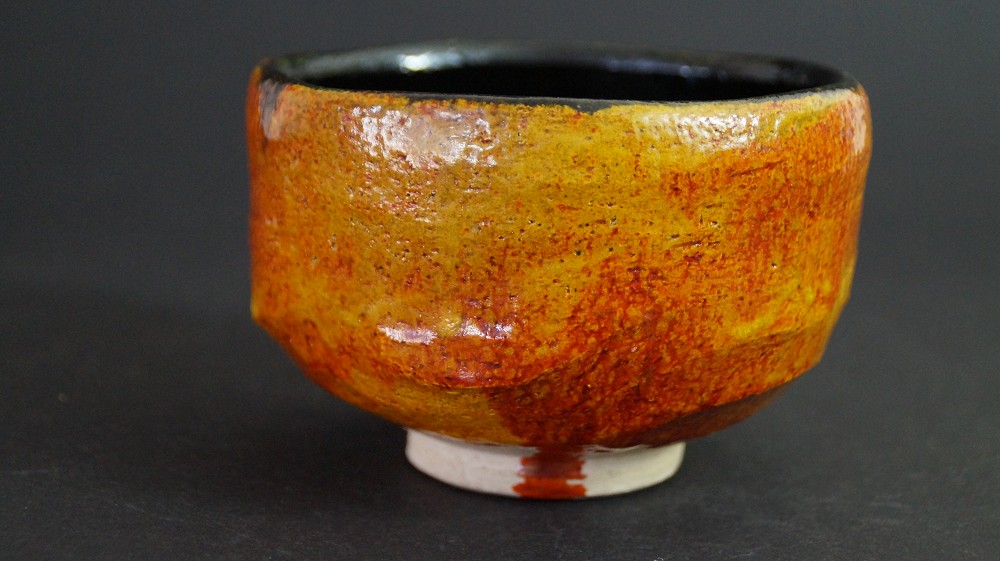 Side view of the chawan made of Tobe ware with amber glaze and black rim on the inside by Haryoku