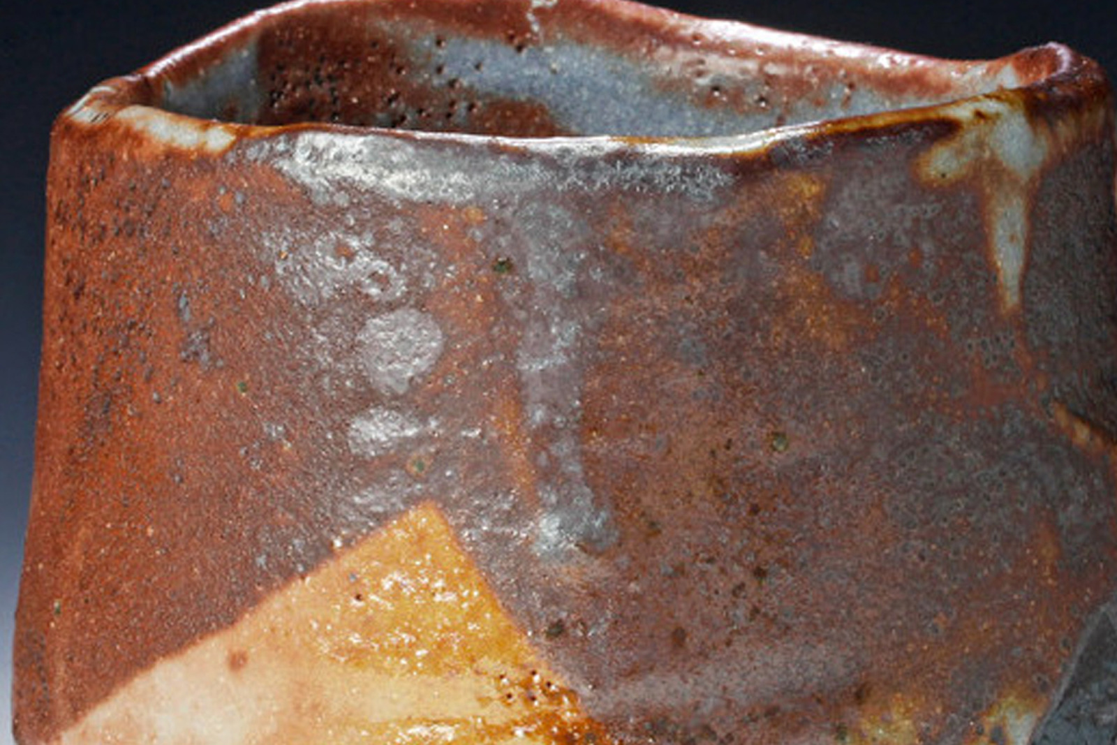 Nahaufnahme einer handgetöpferten Teeschale (Chawan) aus Steinzeug mit erdbraun bis ockerfarben changierender Glasur, grauen Glasurschlieren und körniger Oberfläche