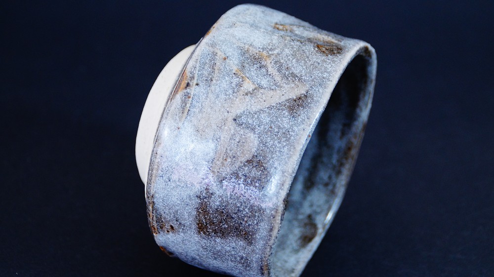 Tilted side view of the chawan made of Shino ware by Kazufumi Wada showing the unglazed foot