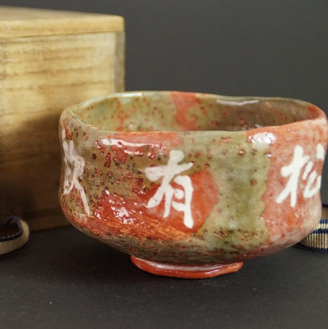 Chawan mit Schriftzeichen in der Glasur vor der unscharf sichtbaren Aufbewahrungsbox