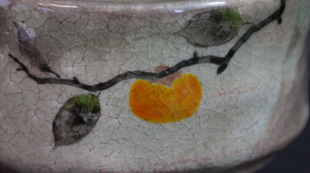 Close-up of the hand-painted persimmon branch with orange fruit and green leaves on the chawan made of Kyoto ware