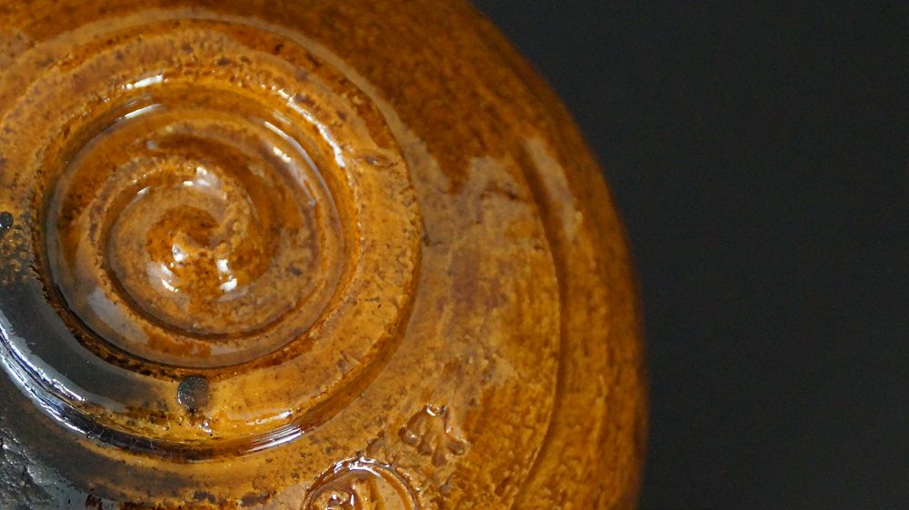 Weitere Nahaufnahme des spiralfoermig gedrehten Standfusses mit Kuenstlersiegel der Chawan Teeschale aus Ohi-Keramik