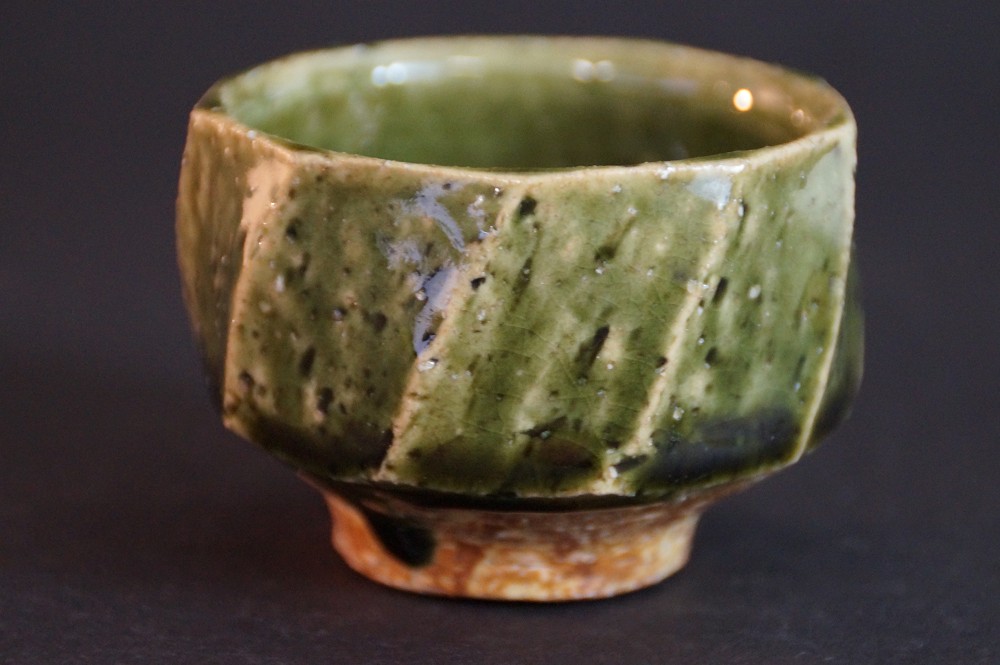 Frontalansicht der handgetoepferten Oribe Sake Schale mit facettierten Wandungen und kupfergruener Glasur