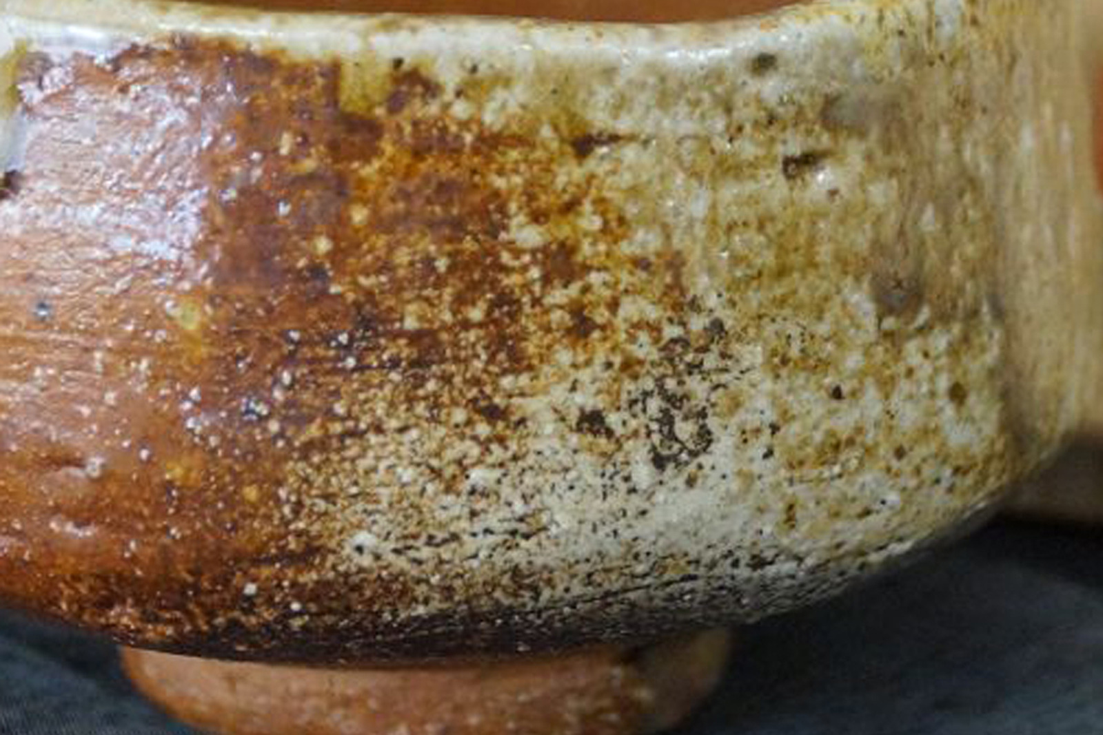Close-up of the wall of a Shigaraki ware tea bowl with a rough, ash-covered surface, reddish-brown fire zone, and foot ring