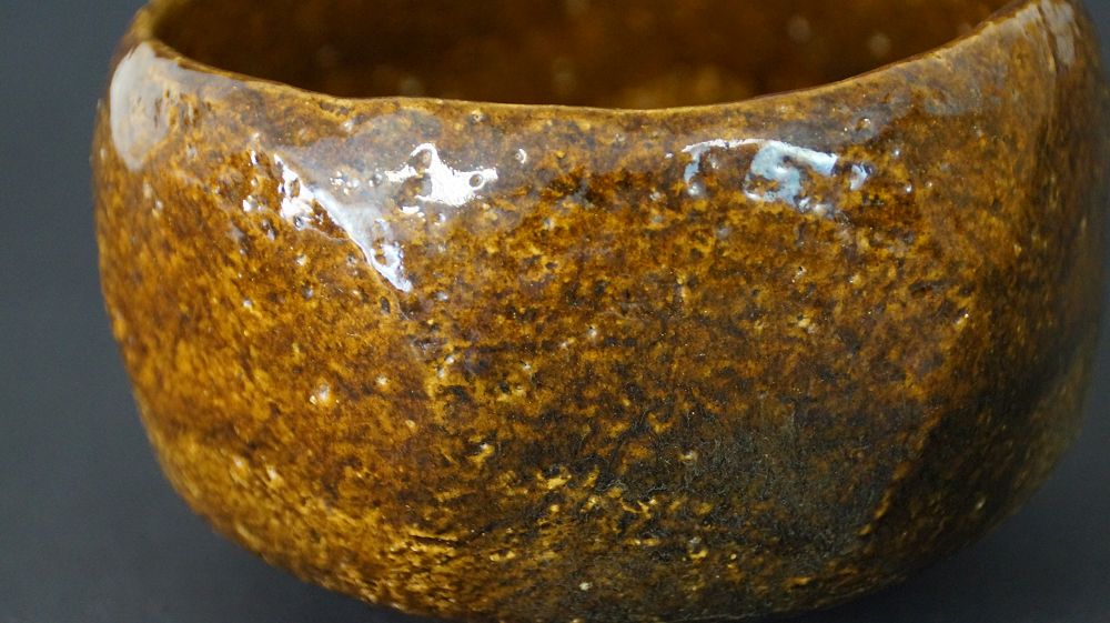 Extreme Nahaufnahme der gesprenkelten braunen Glasurstruktur der Chawan Teeschale aus Raku-Keramik