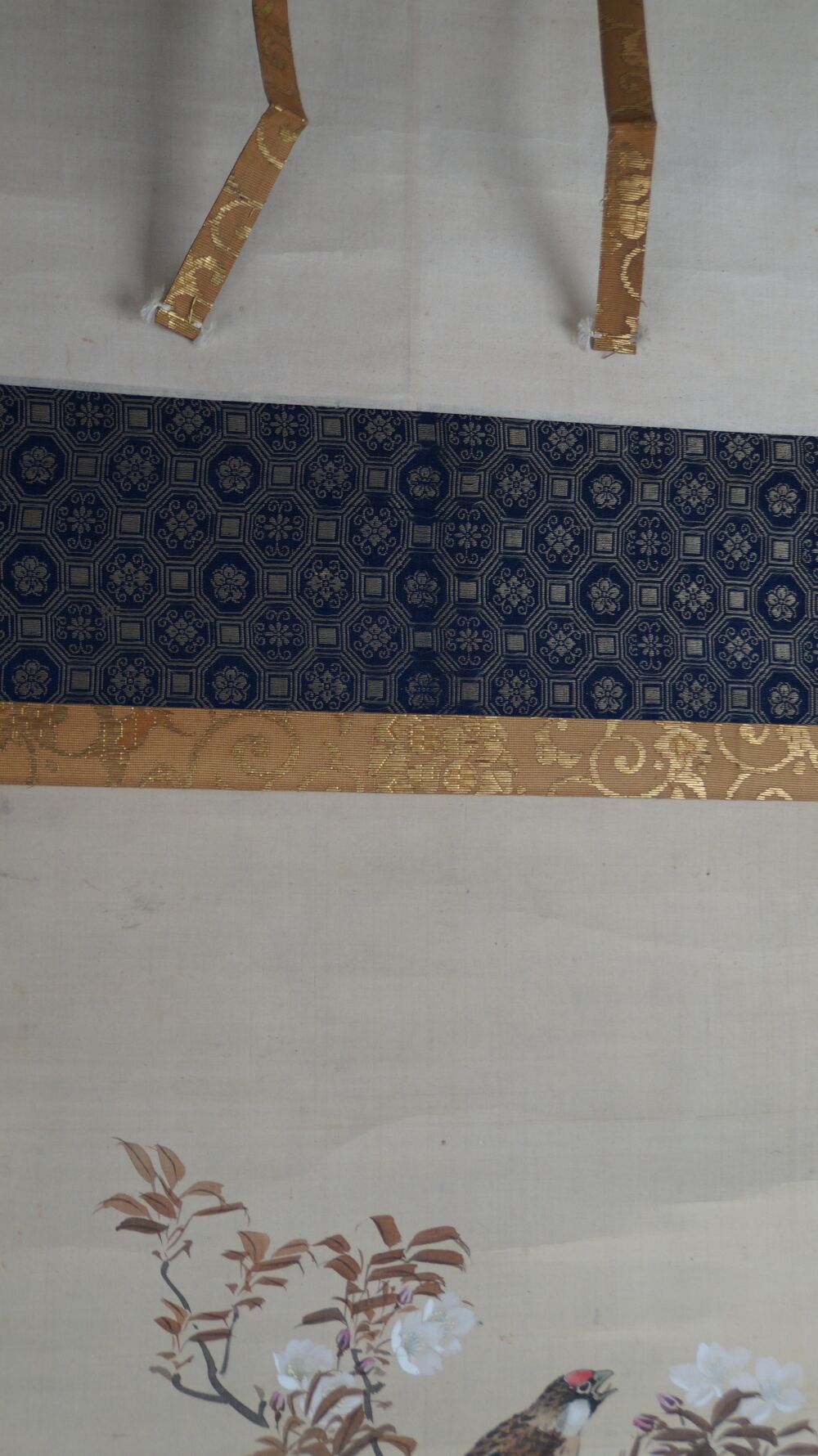 Detail view of the dark blue brocade mounting with golden vine border and hanging cords of the hanging scroll Singing Bird in Cherry Blossom Branch