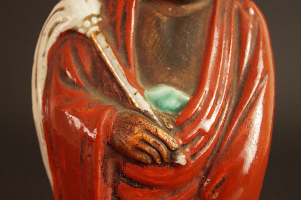 Bodhidharma Daruma figure made of red Kutani porcelain close-up of folded hands with robe folds motif close-up