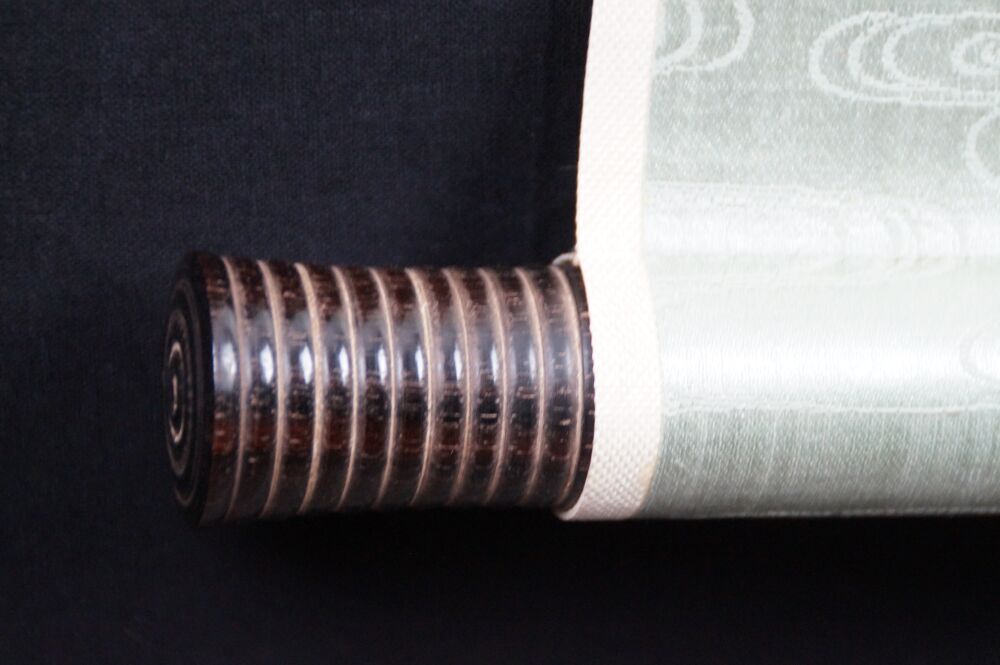 Detail view of the scroll end with dark wooden knob and cloud-pattern silk of the Kakemono