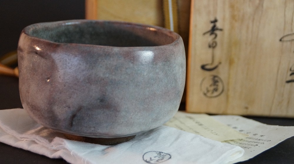 Side view of the chawan made of Ohi ware in front of the inscribed storage box by Kaihatsu Bunmei