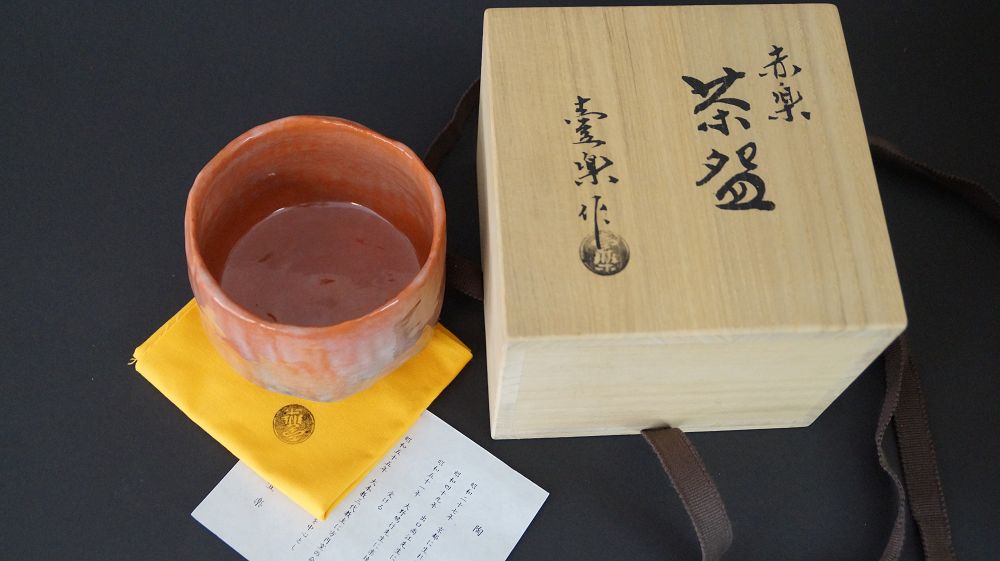 Chawan tea bowl with tea next to the labeled storage box Akaraku Chawan and handwritten certificate of authenticity
