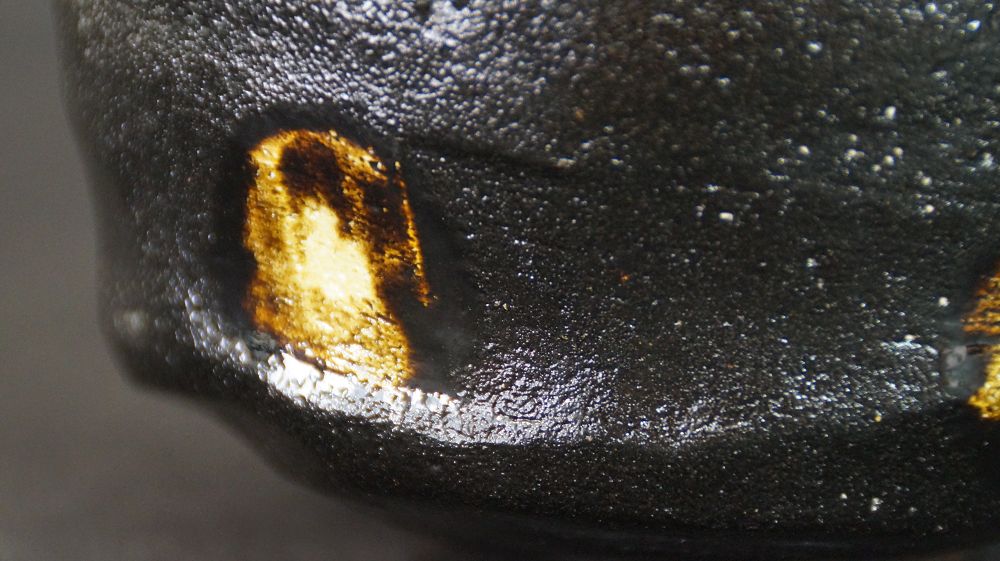 Extreme close-up of the golden glaze spot on the black glaze of the chawan made of Raku ware