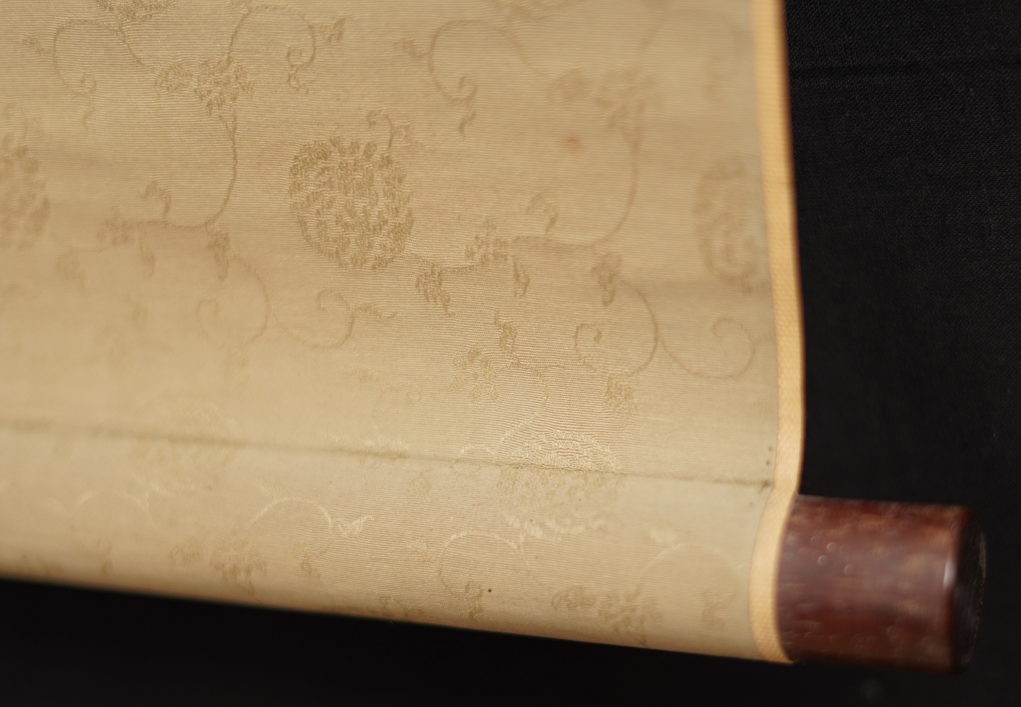 Detail view of the scroll end with dark wooden knob and gold-colored silk of the kakemono songbird on blossoming cherry branch