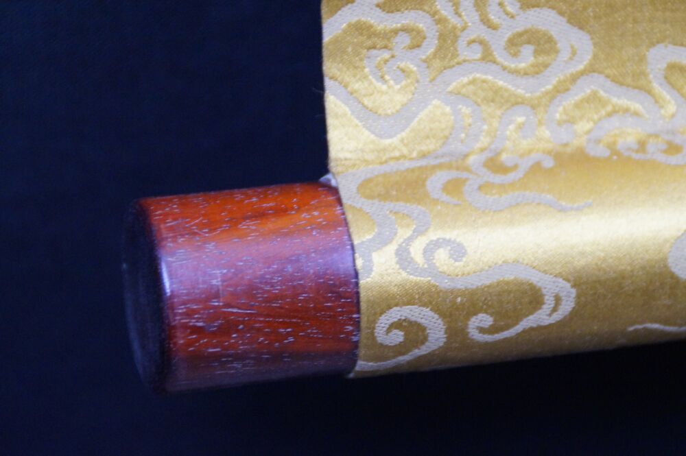 Detail view of the scroll end with reddish-brown wooden knob and gold brocade silk of the hanging scroll