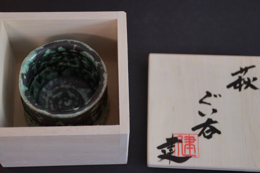 The sake cup lying in the opened storage box next to the lid with calligraphy