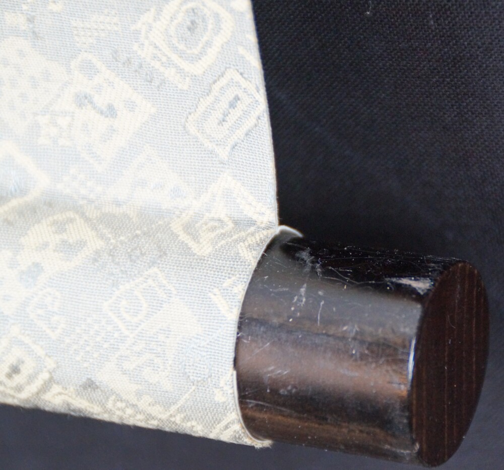 Close-up of the dark scroll end with gray-gold brocade mounting on one of the three triptych prints after Miyamoto Musashi