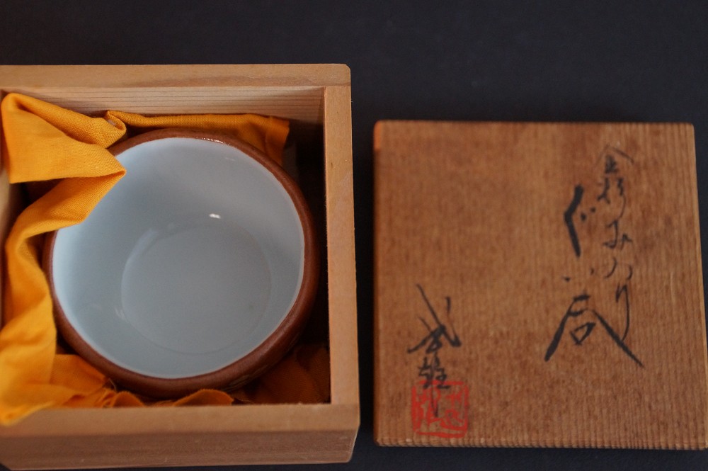 The sake bowl wrapped in orange cloth lying in the opened storage box next to the lid