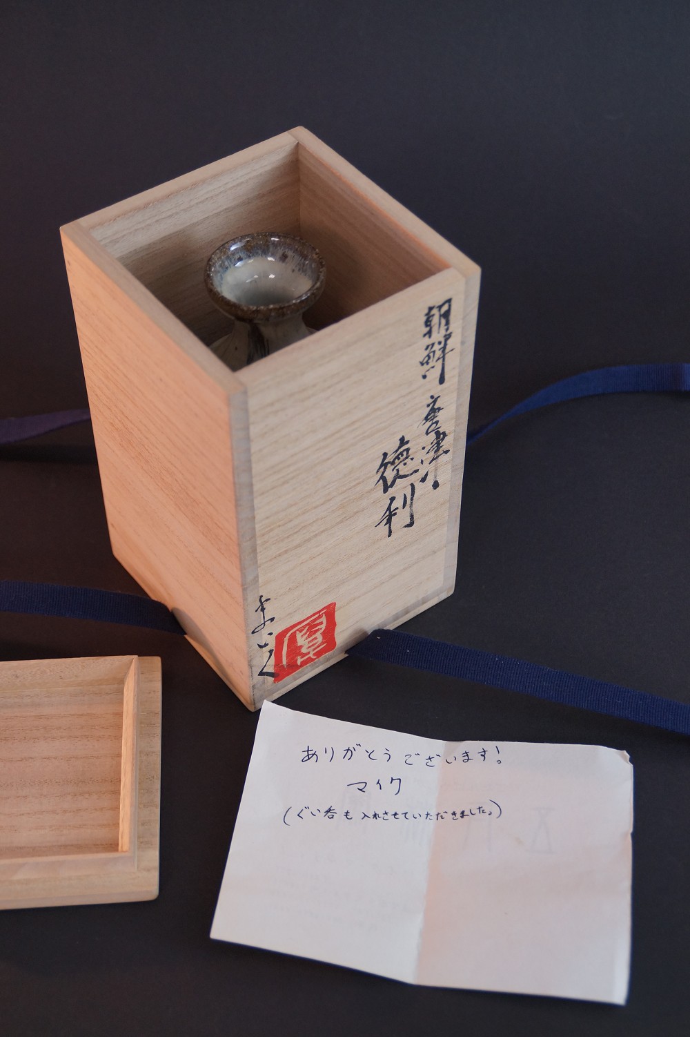 The sake bottle standing in the opened storage box with a personal thank-you note from the potter