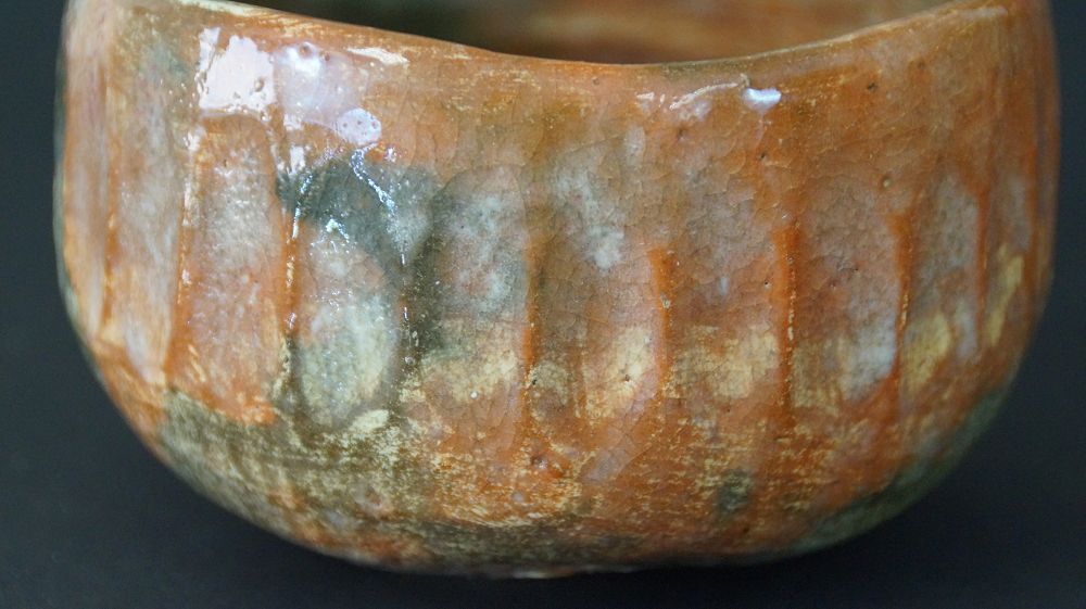 Close-up of the ribbed rim with orange-green Raku glaze of the chawan tea bowl made of Raku ware