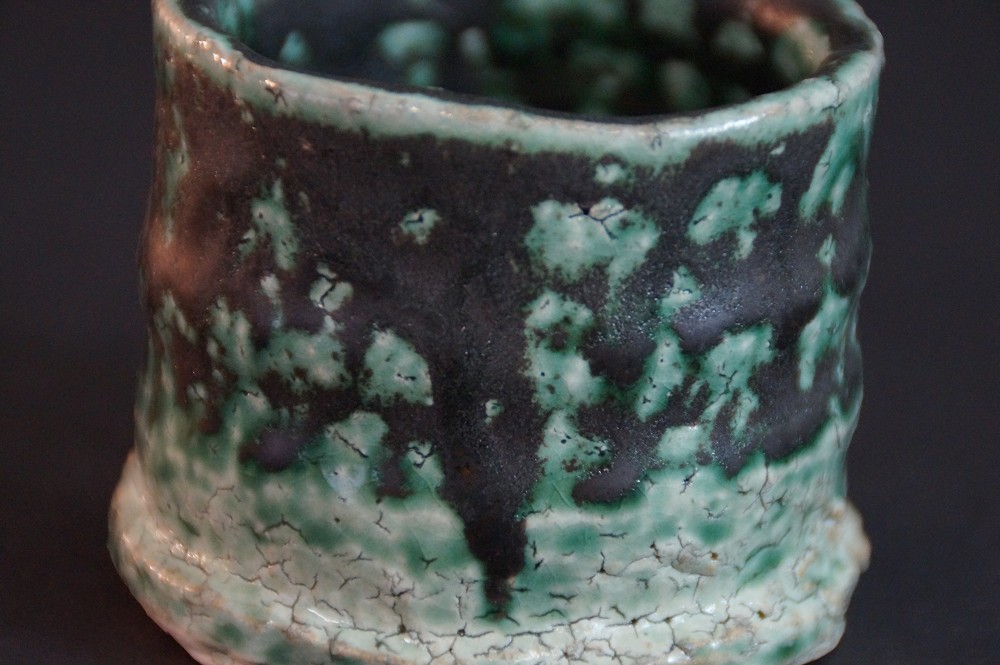 Extreme close-up of the crackled green-black mottled glaze surface