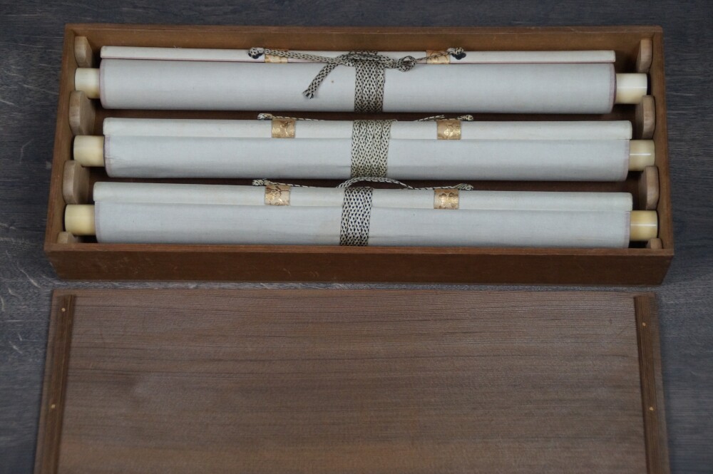 Alle drei zusammengerollten Kakemono des Sets Wasser, Rueckzug und Aufstieg mit elfenbeinfarbenen Rollenenden in der geoeffneten Aufbewahrungsbox
