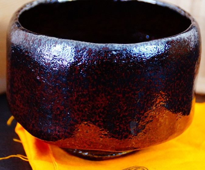 Chawan made of Raku ware by Shoraku Sasaki with reddish-brown and black mottled glaze in front of the storage box