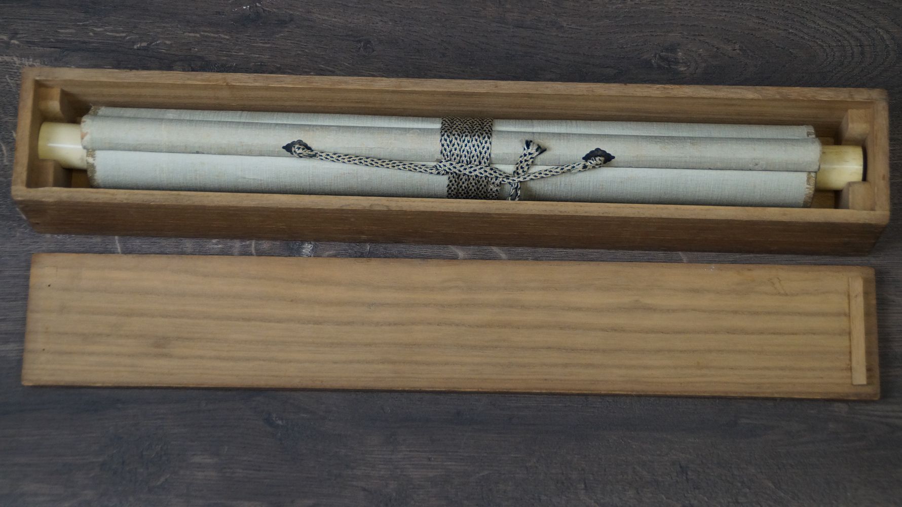 Zusammengerolltes Kakemono Verschneites Kloster am stillen See mit elfenbeinfarbenen Rollenenden in der geoeffneten Aufbewahrungsbox
