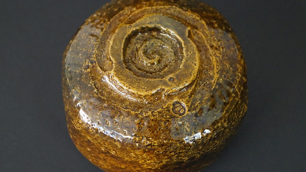Detailansicht des spiralfoermig gedrehten Standfusses mit eingepraegtem Kuenstlersiegel der Chawan Teeschale aus Raku-Keramik