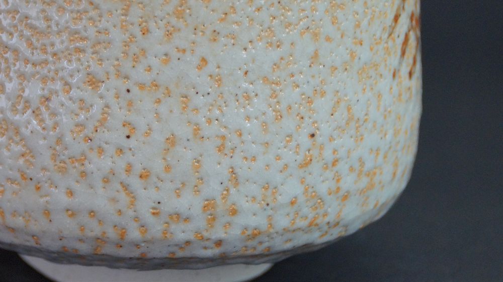 Extreme close-up of the textured white Shino glaze with orange fire trace