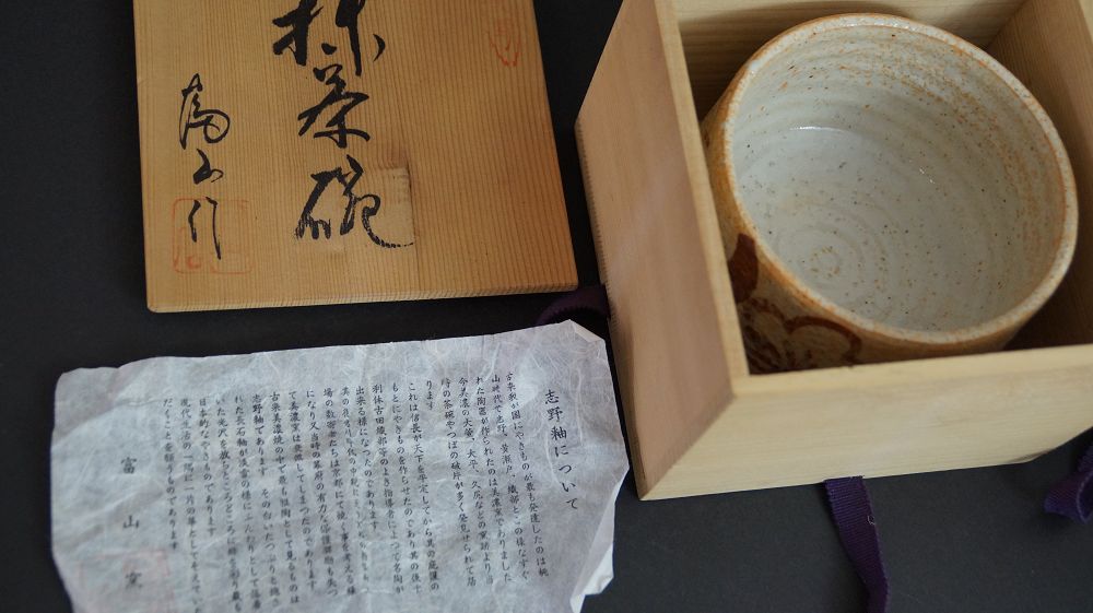 Chawan of Shino ware in the opened storage box next to the box lid and the certificate of authenticity for the Toyama kiln