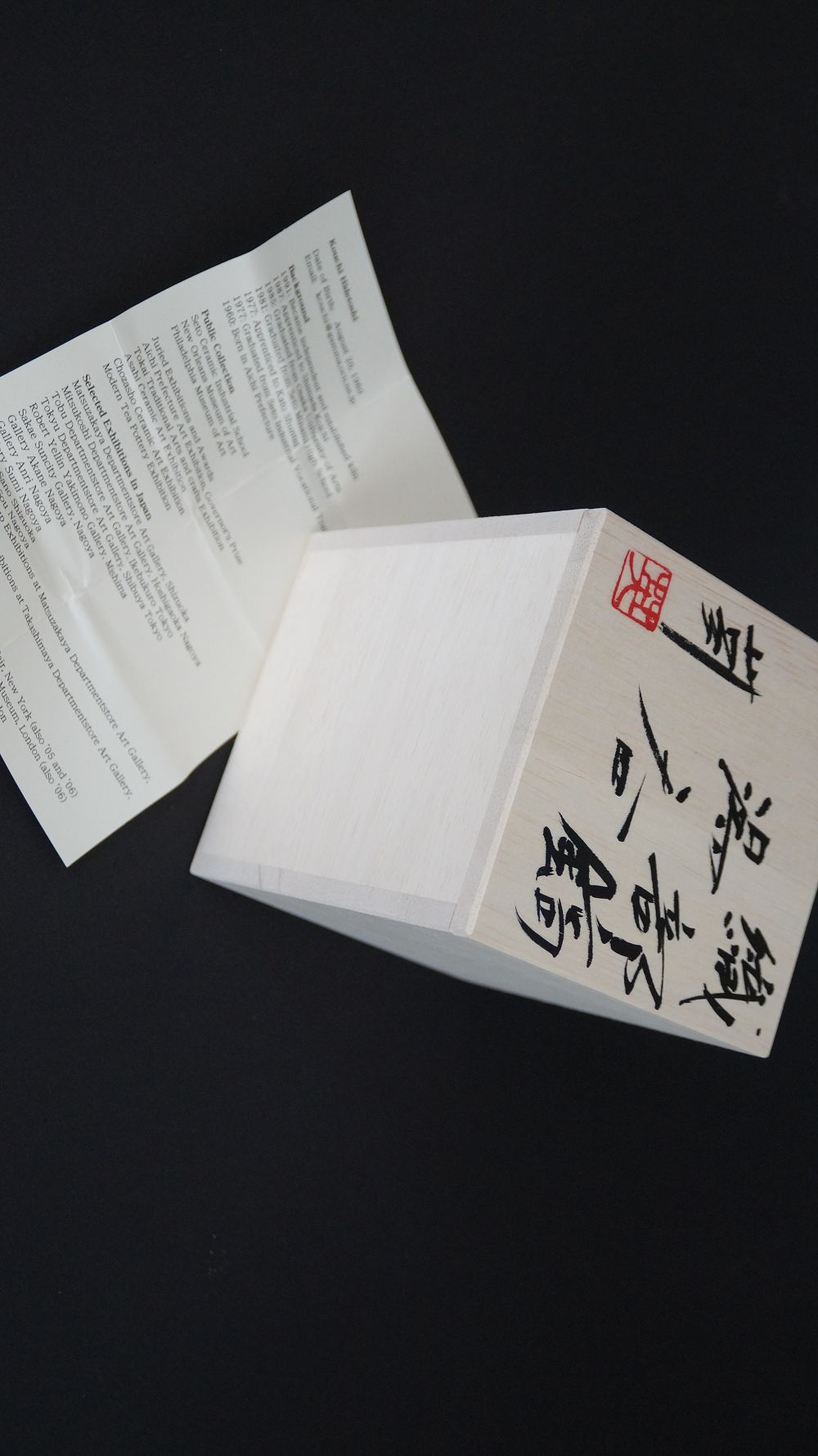 Signed box lid with red artist's seal next to the artist biography of the yunomi tea bowl made of Oribe ware