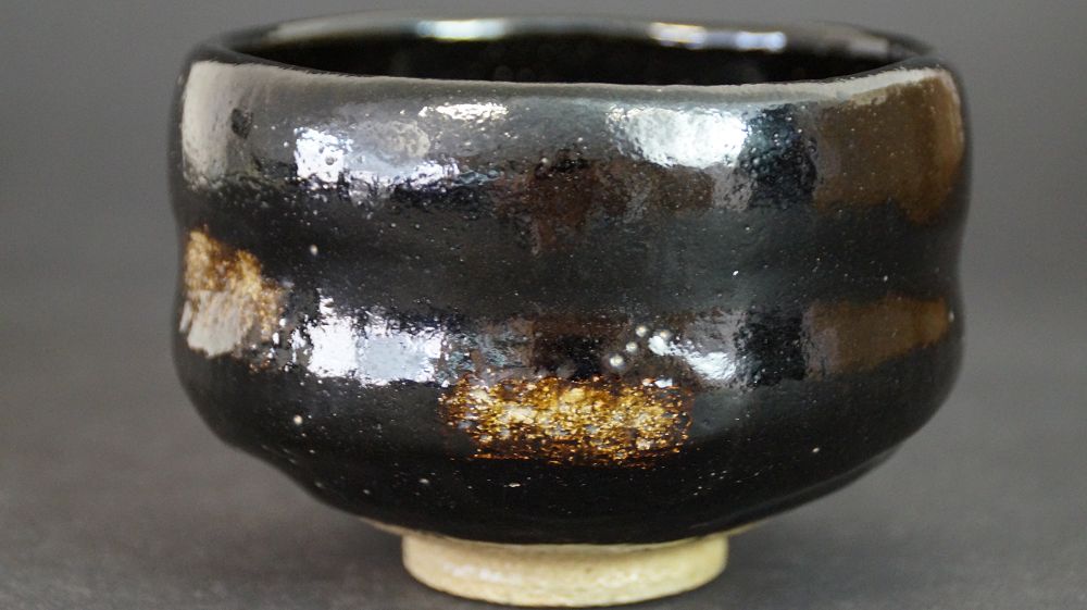 Another view of the chawan made of Raku ware with black glaze and gold-colored glaze spots at the rim