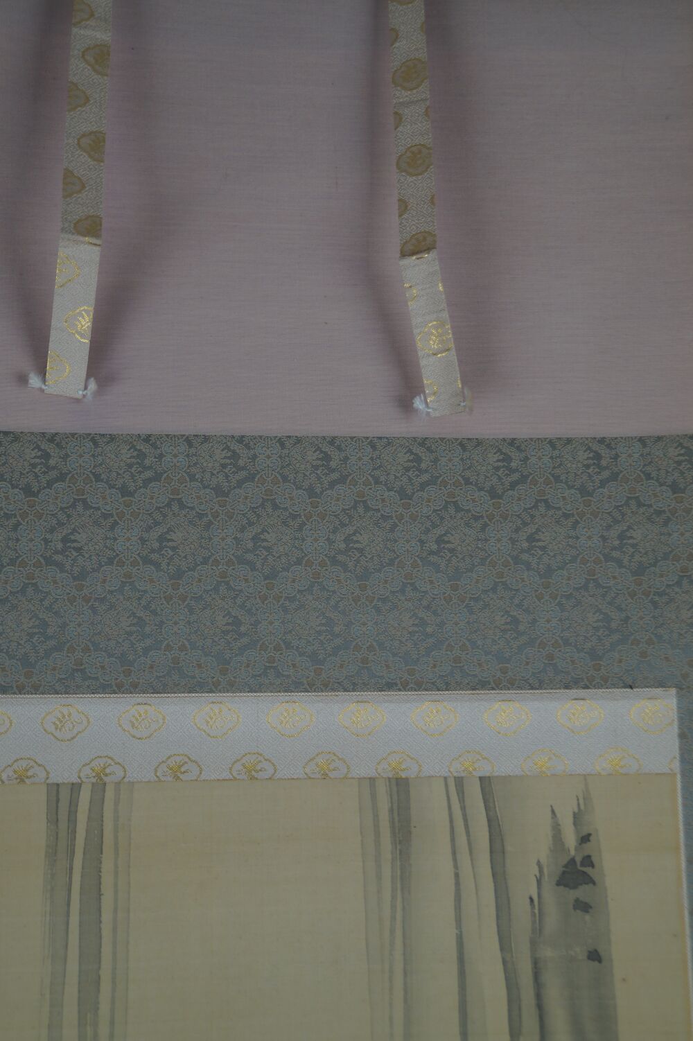 Detail view of the pink silk mounting with golden pattern and hanging cords of the hanging scroll Koi at a Waterfall