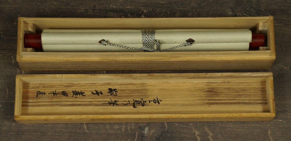 Das zusammengerollte und mit Kordel verschnuerte Kakemono liegend in der geoeffneten Aufbewahrungsbox