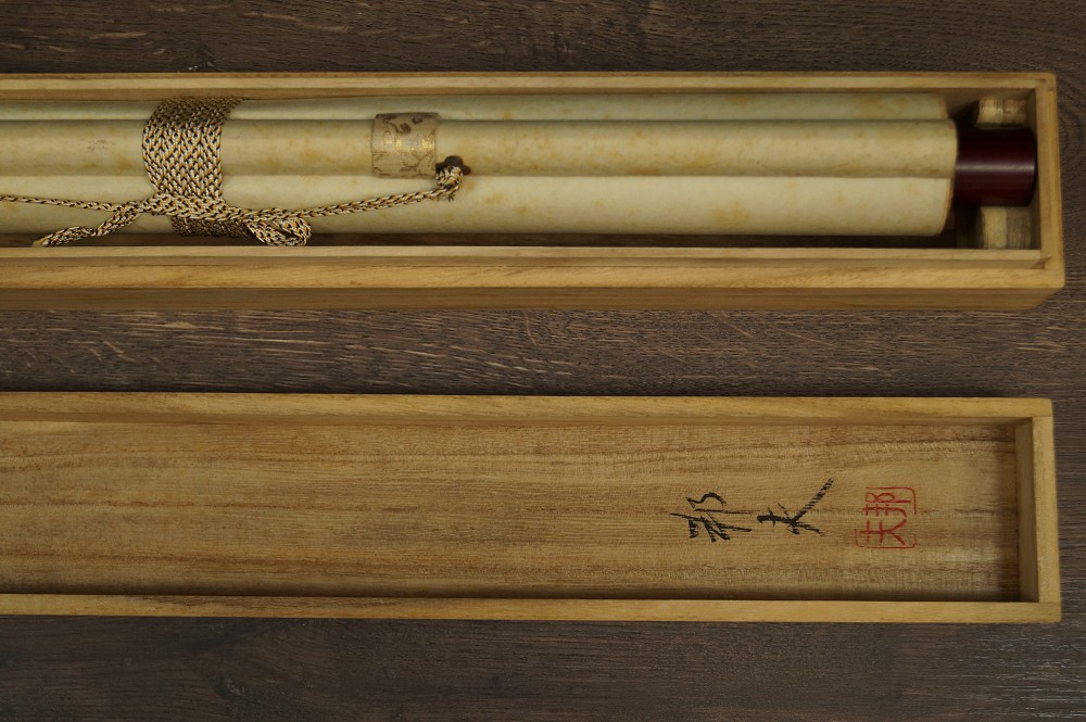 Rolled-up hanging scroll in opened wooden box with cord