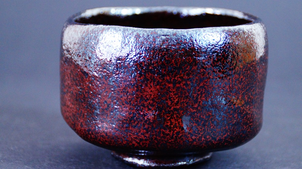 Side view of the chawan made of Raku ware by Shoraku Sasaki with irregular walls and a mottled reddish-brown and black glaze