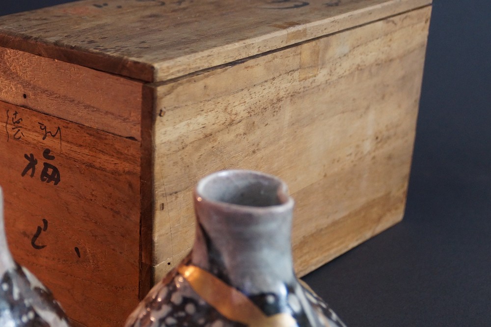 Close-up of the bottle neck with the storage box faintly visible in the background, bearing calligraphy