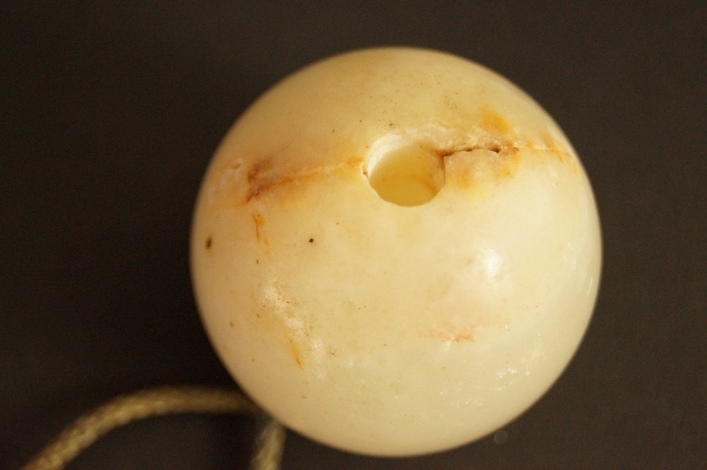 Light-colored stone sphere with drilled hole and reddish-brown spots Stone Close-Up 1