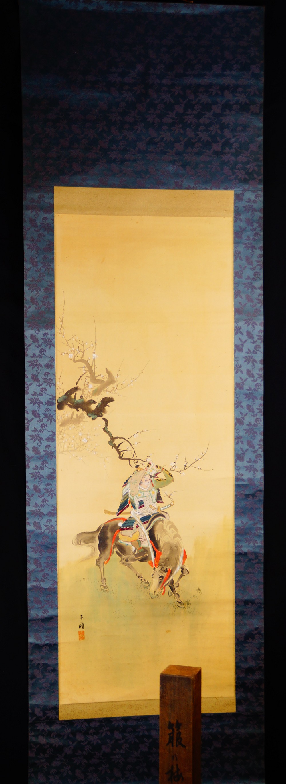 Full view of the kakemono with the mounted samurai warrior beneath plum blossoms, hung on a wooden stand