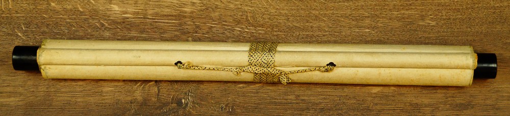 Rolled-up hanging scroll with cord and wooden jikusaki on a wooden table