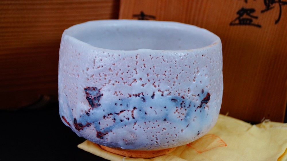 Chawan made of Shino ware by Jyuzo Sato in front of the storage box on a yellow cloth