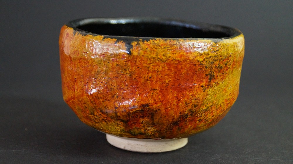 Side view of the chawan made of Tobe ware with amber glaze and black rim on the inside by Haryoku