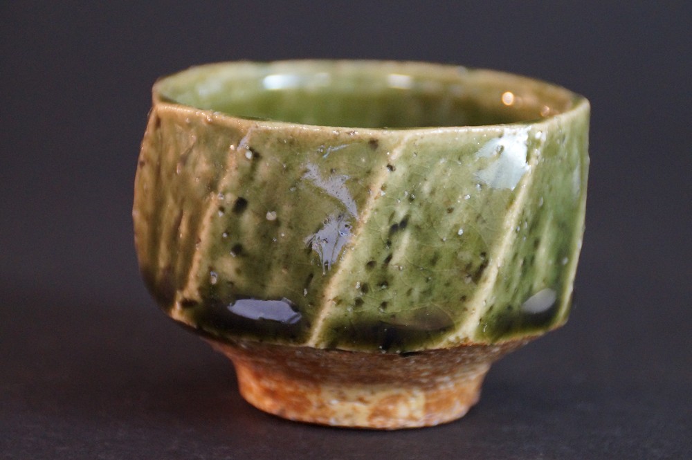 Side view of the faceted sake bowl with copper-green glaze over cream-colored shard