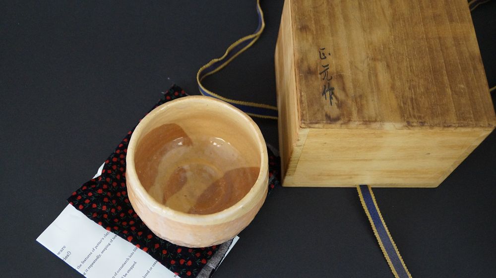 Chawan tea bowl on patterned cloth next to handwritten certificate of authenticity and signed box lid