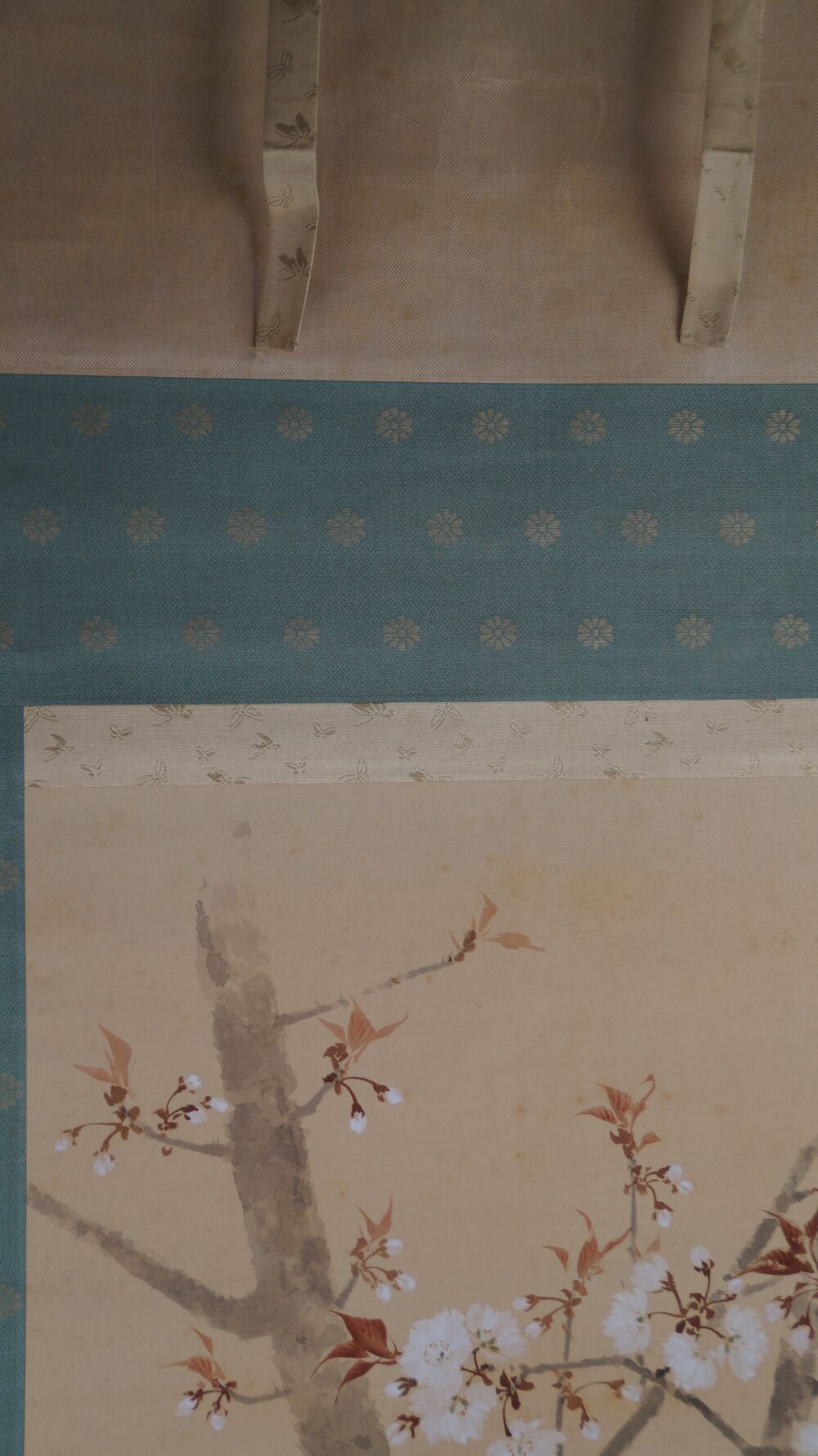 Detail view of the turquoise silk mounting with blossom pattern and hanging cords of the kakemono Spring at the Old Cherry Blossom