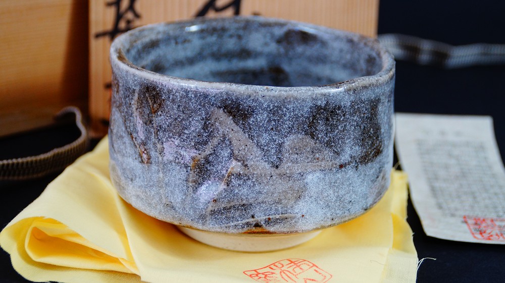 Side view of the chawan made of Shino ware by Kazufumi Wada next to the storage box with certificate of authenticity