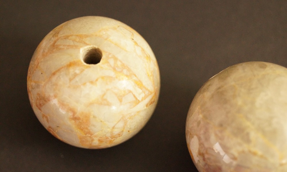 Two beige marbled stone spheres one with a drilled hole stone close-up 1