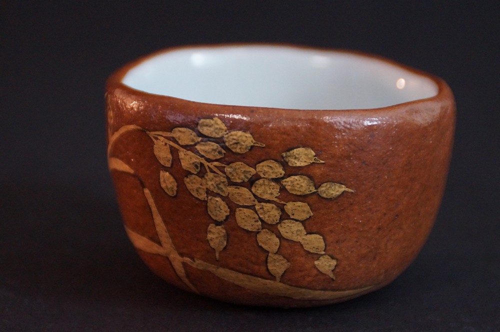 Another side view with gold-colored branch motif on reddish-brown clay body
