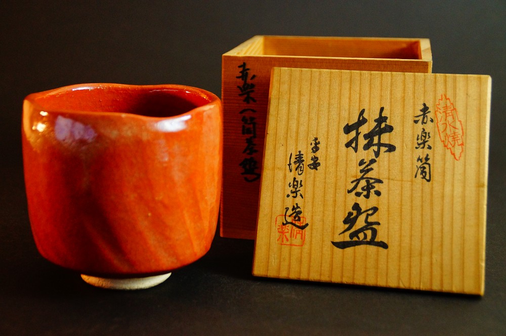 Chawan aus rot glasierter Raku-Keramik neben der beschrifteten Aufbewahrungsbox von Seiraku